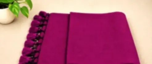 A deep berry pink mulmul saree folded on cream cloth with tonal pink tassels.