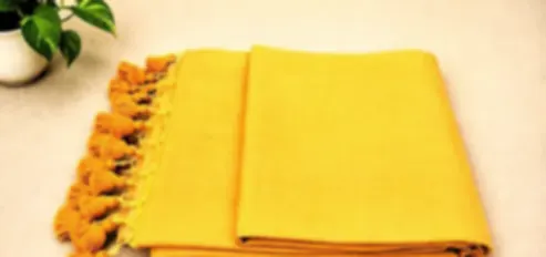 A warm golden yellow mulmul saree folded on cream cloth with orange tassels.