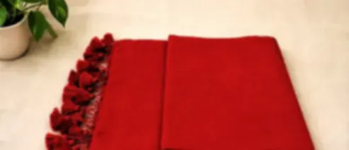 A saturated red mulmul saree folded on cream cloth with matching red tassels along its edge.