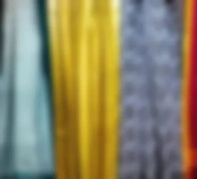 Yellow, teal and indigo printed drapes hanging in a row above stacks of folded sarees.
