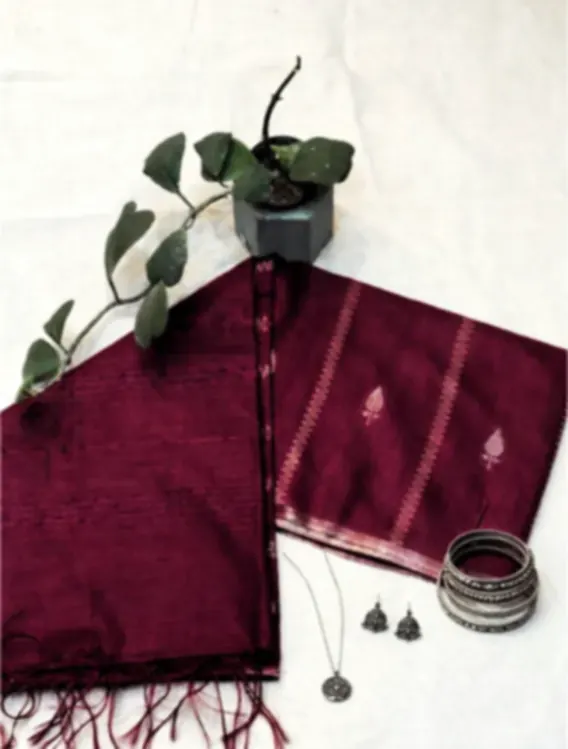 A magenta silk blend saree with a zari border and tasselled end, folded on white cloth with bangles.