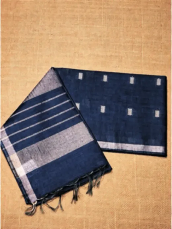 A steel blue silk blend saree with silver zari stripes and small woven motifs, folded on an ochre backdrop.