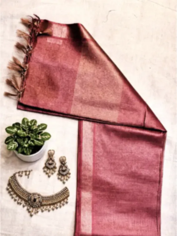 A rose tissue saree with a wide silver border and fringe, folded beside pearl earrings and a necklace.
