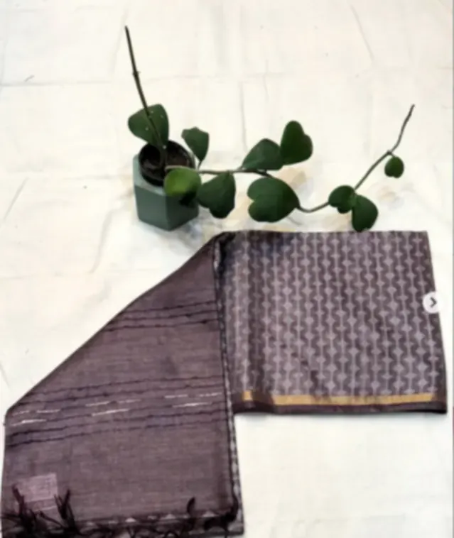 A mauve tussar blend saree with a fine printed border, folded on white cloth beside a eucalyptus sprig.