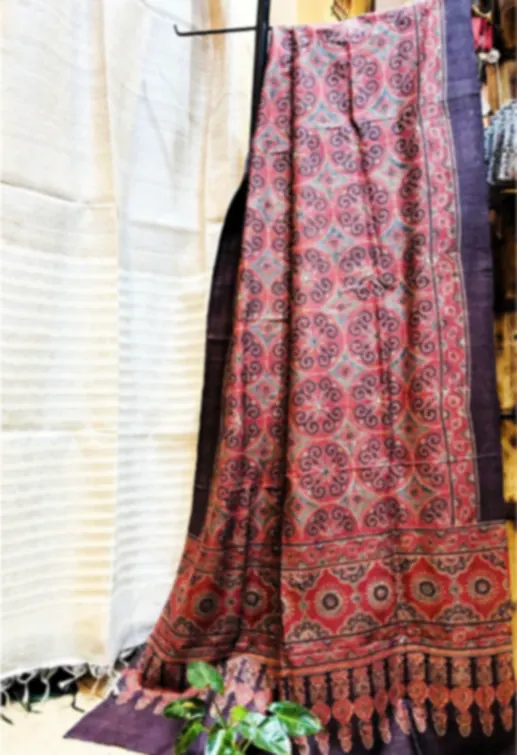 A pure tussar dupatta printed with Ajrakh motifs in earthy reds and blues, hanging in the shop.