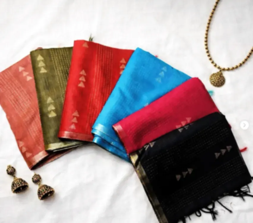Five tussar sarees in rust, olive, red, blue and black, fanned out to show their woven motifs, with jhumkas beside them.