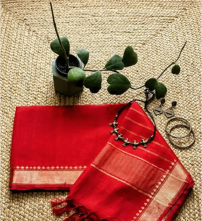 A red viscose saree with a gold zari border and fringe, laid on woven jute with bangles and a necklace.