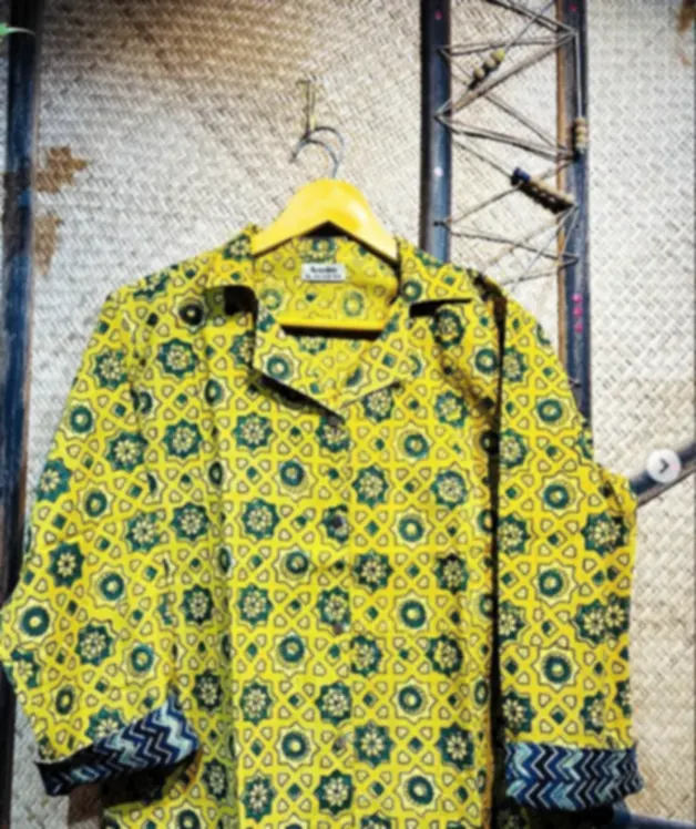 Mustard yellow Ajrakh shirts with indigo contrast cuffs, hanging together against a woven backdrop.
