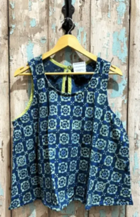 An indigo hand block printed sleeveless cotton top on a hanger against weathered blue wood.
