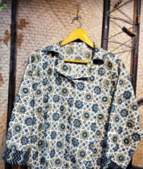 An ivory cotton shirt with intricate blue Ajrakh patterns and a chevron contrast cuff, on a hanger.
