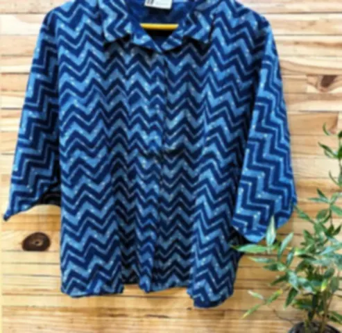 A blue cotton shirt in a patchwork-style Dabu print with different depths of indigo, on a hanger.