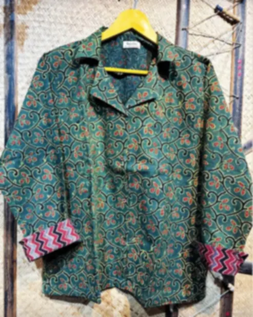 A forest green cotton shirt layered with Ajrakh scrollwork, on a hanger against a woven backdrop.