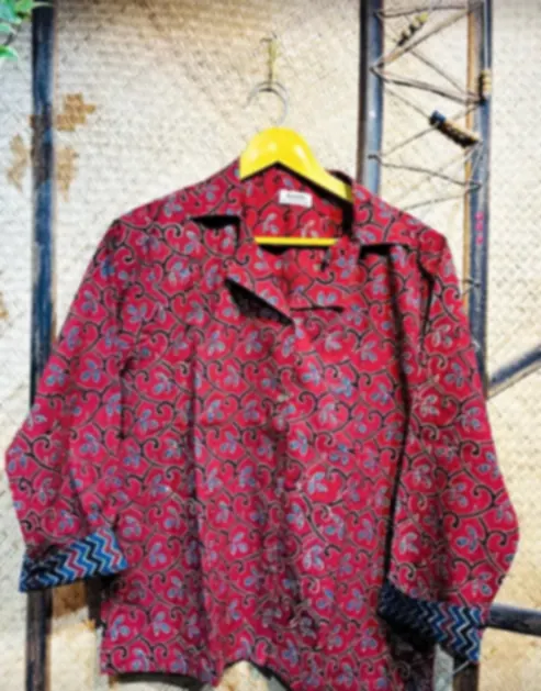 A garnet red cotton shirt printed with traditional Ajrakh florals, on a hanger.