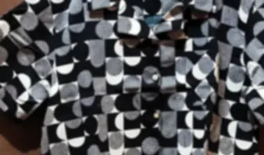 A shirt in bold monochrome geometry on soft lightweight cotton, on a hook against a rust wall.