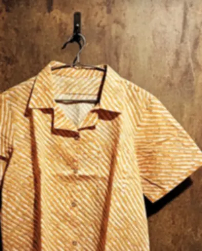 A shirt in diagonal mustard lines on breathable cotton, cut for easy movement, on a hook.