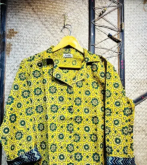 A mustard yellow cotton shirt with a repeating Ajrakh medallion print and contrast indigo cuffs, on a hanger.